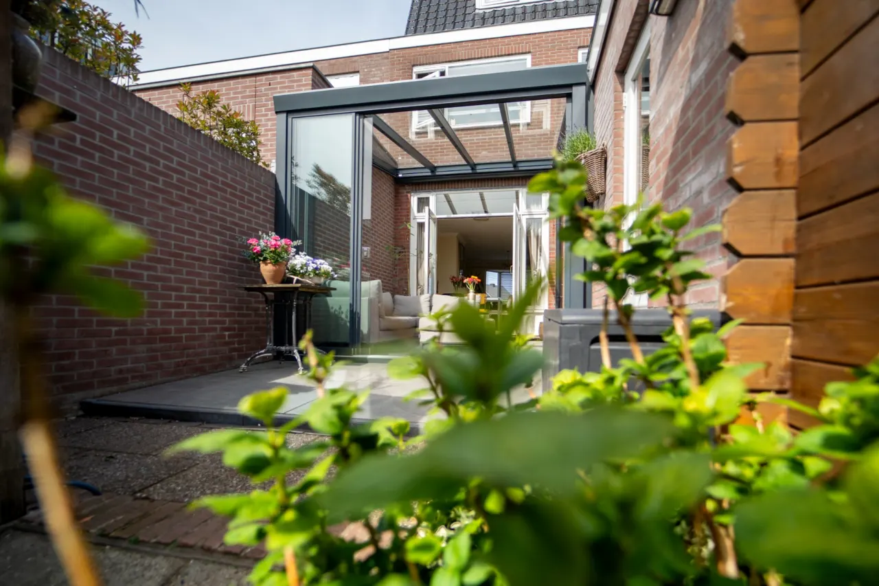 Aluxe Trendline overkapping aan een bakstenen woning, met open glazen schuifpui